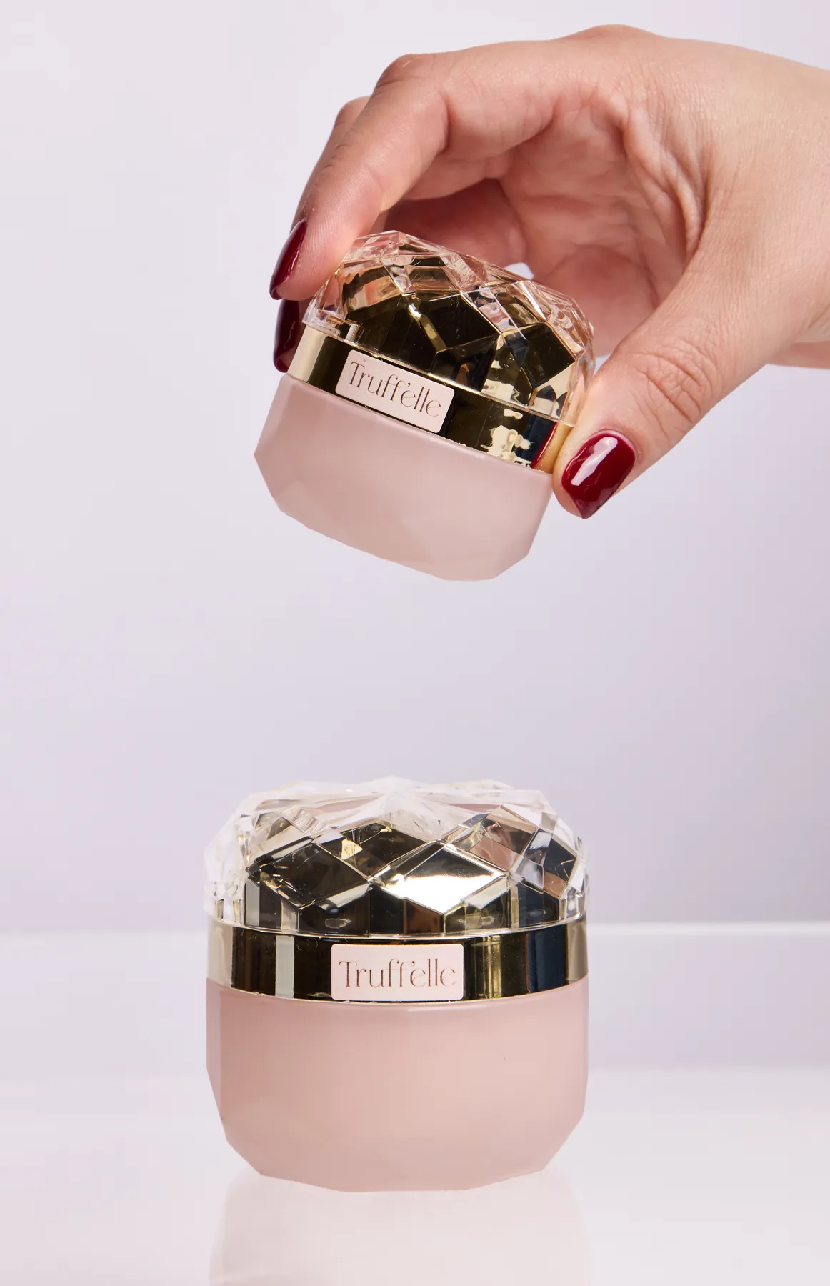 A hand lifting The Eye Cream above a jar of The Peptide Cream